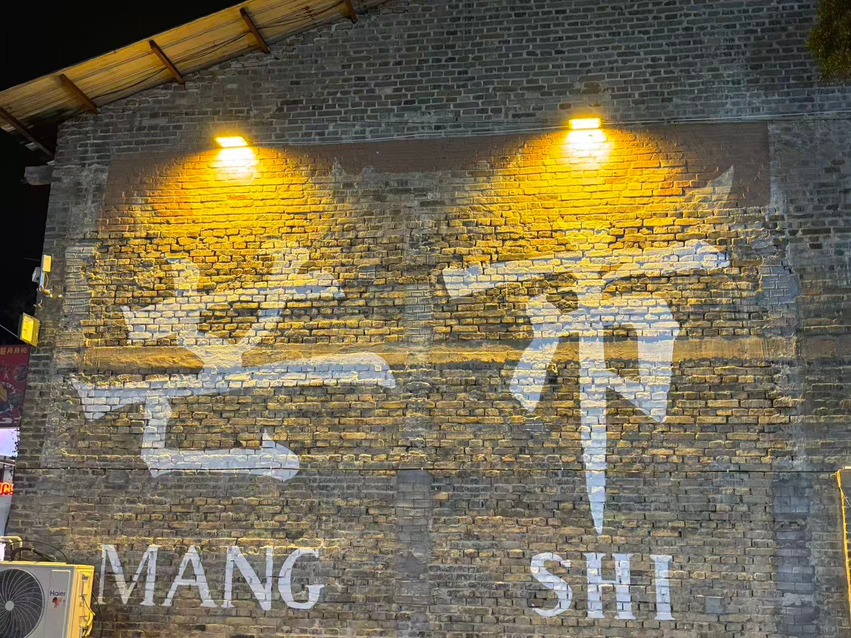 夜间灯光照亮写着芒市的砖墙